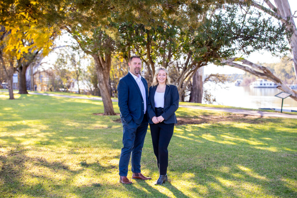 Photo of a two real estate agents, with parklands and river in the background.