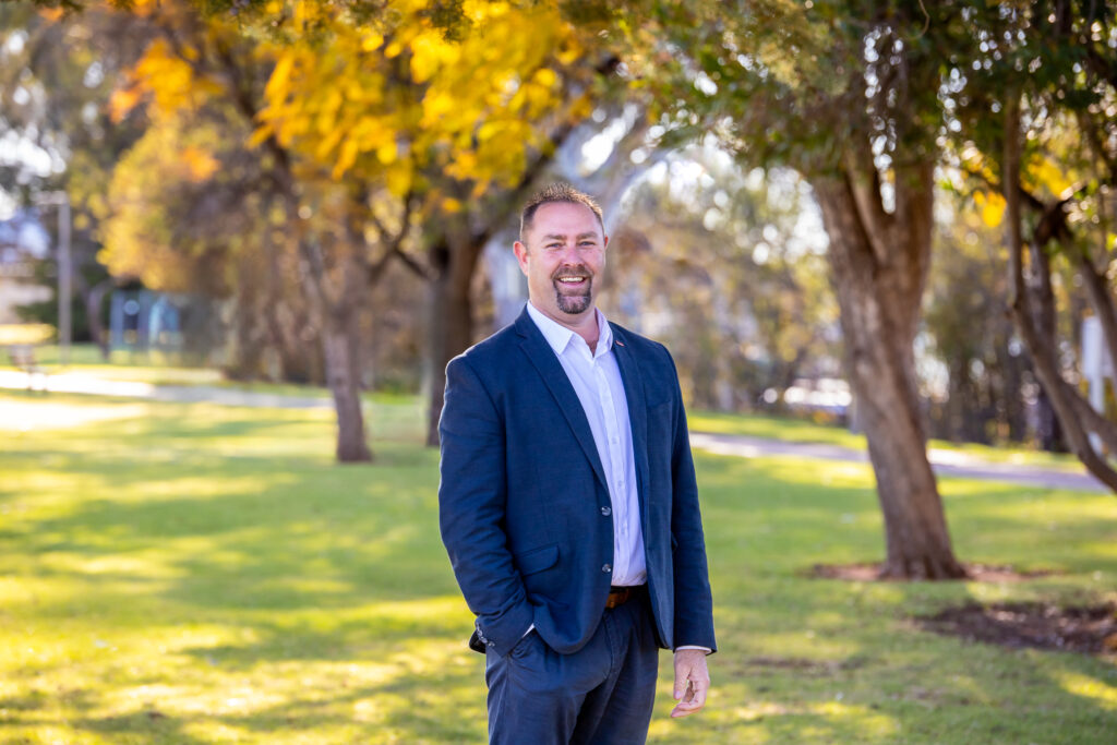 Photo of a male real estate agent, with parklands and river in the background.