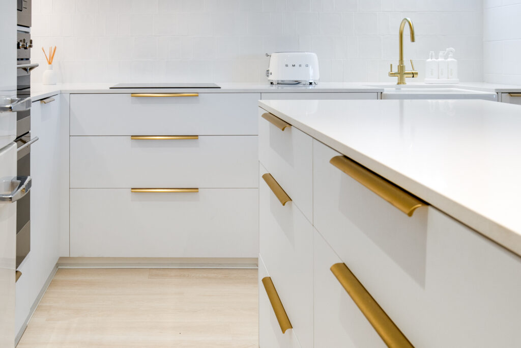 Photo of a newly renovated kitchen. White cabinets with gold handles.